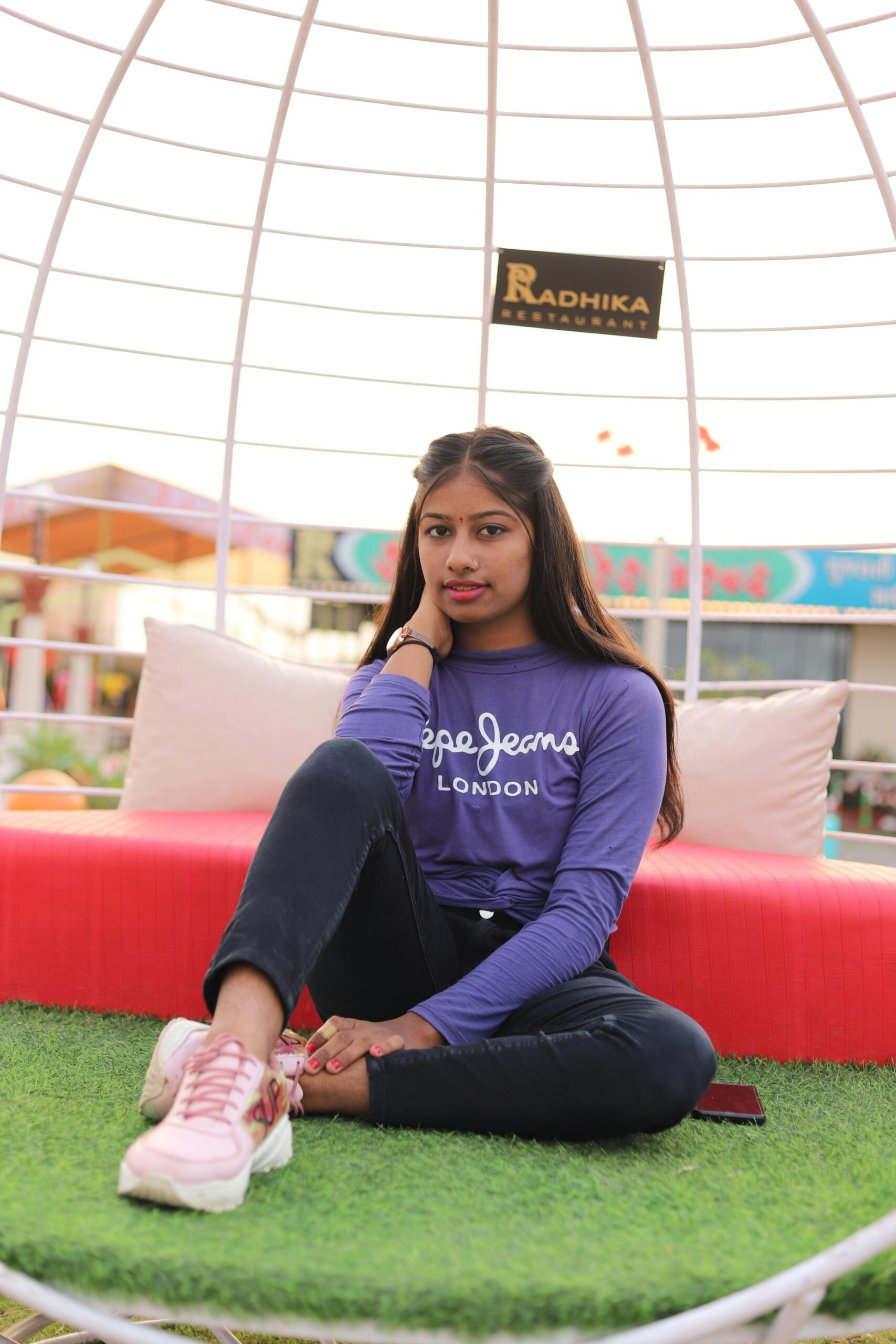 Woman sitting elegantly on grass-covered seat in vibrant outdoor space, Dhari, India.
